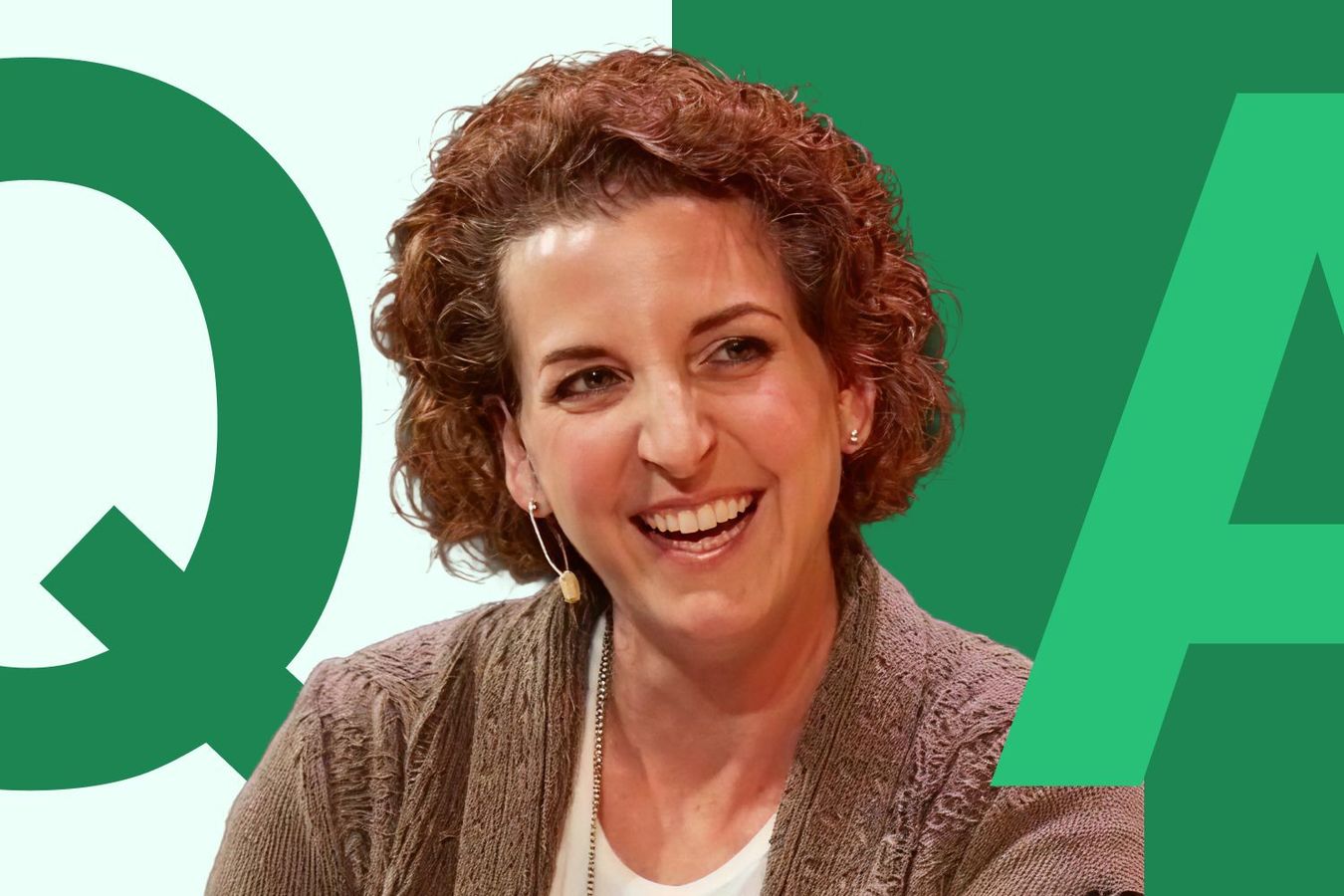Headshot of Nancy Vitale, a woman with shoulder-length curly red hair with a wide smile wearing a beige cardigan and white shirt.
