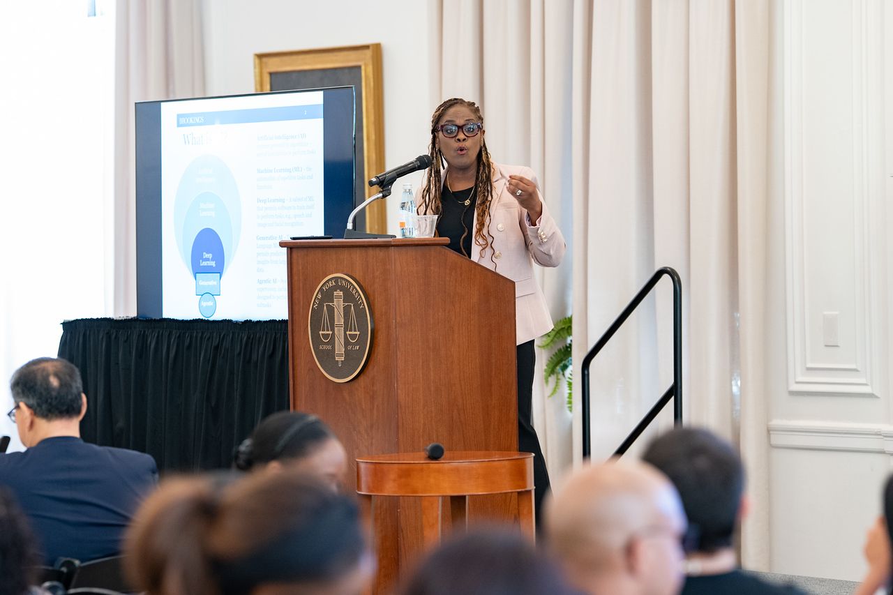 A woman in business attire standing at podium (view is from the audience perspective)